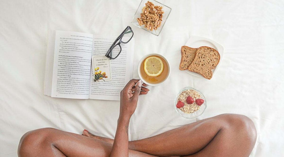 Mujer desayunando en la cama alimentación saludable mientras lee un libro