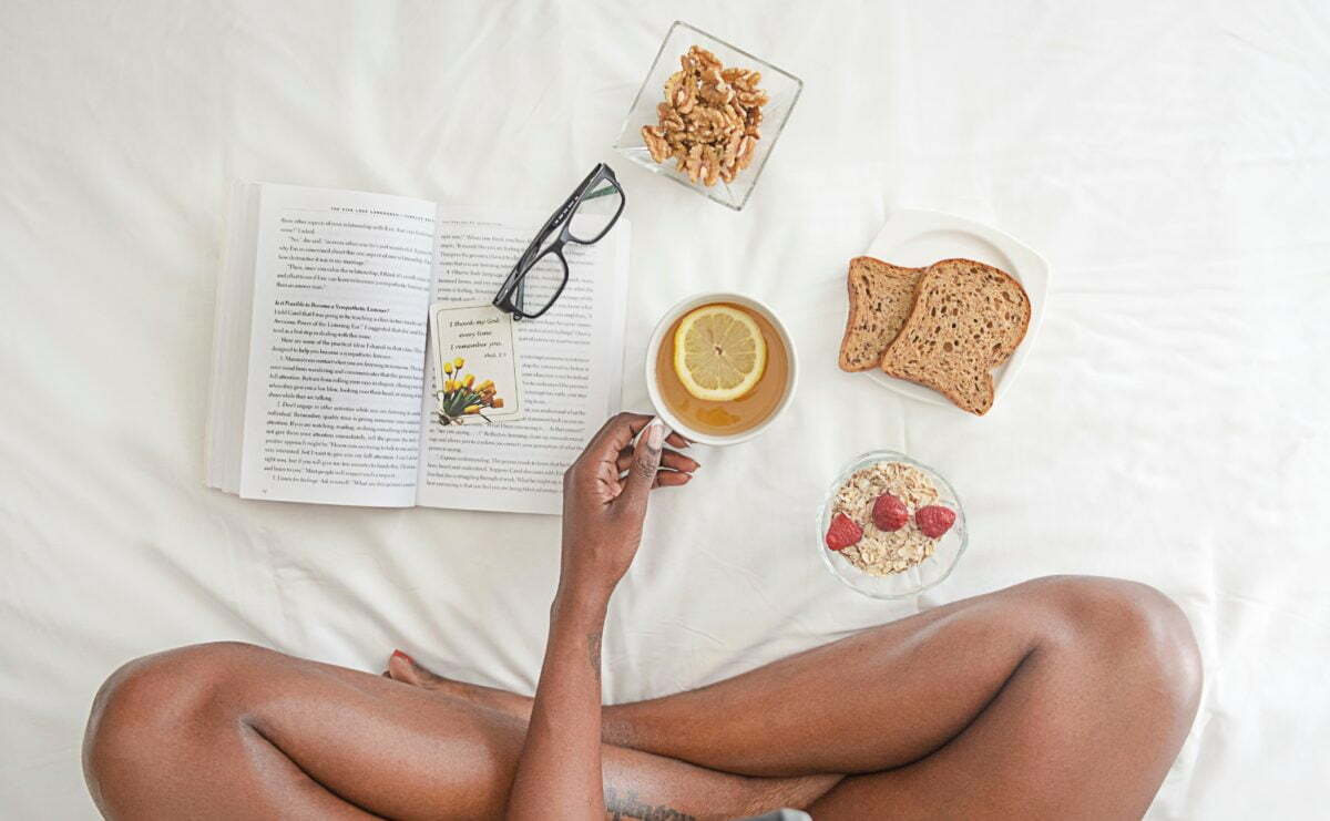 Mujer desayunando en la cama alimentación saludable mientras lee un libro