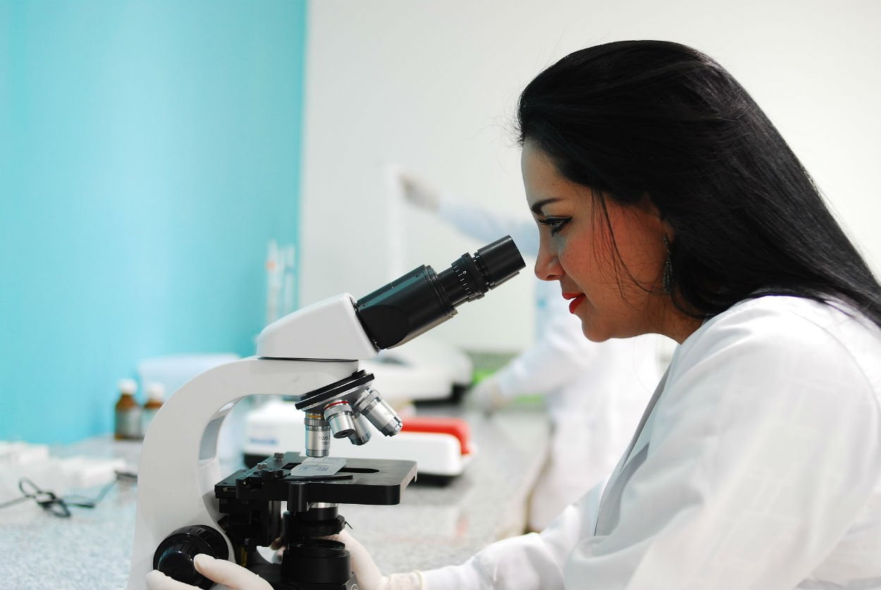 Científica mujer mirando a través de microscopio
